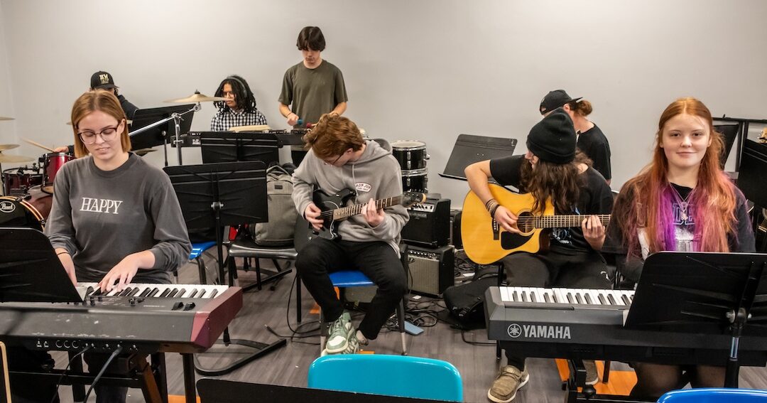 Eight students at Westinghouse Arts Academy charter public high school playing keyboards, guitar and percussion in a classroom ensemble