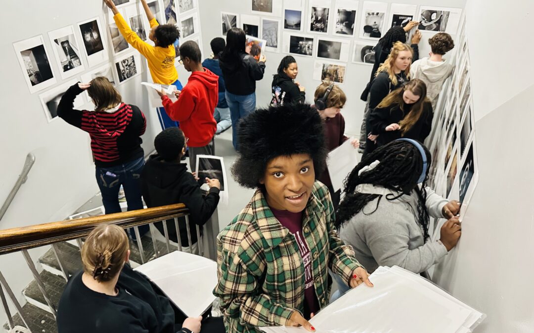 group of WAACS public charter high school students hanging their photography on white walls in a stairwell
