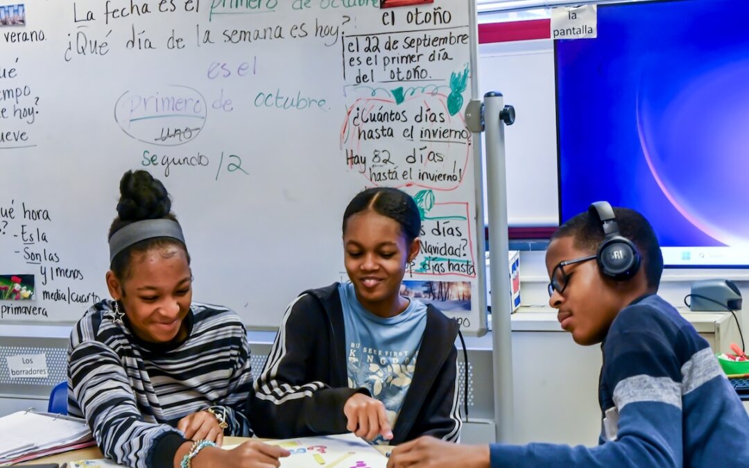 three students at Westinghouse Arts Academy public school talking together while seated in front of a white board in a classroom
