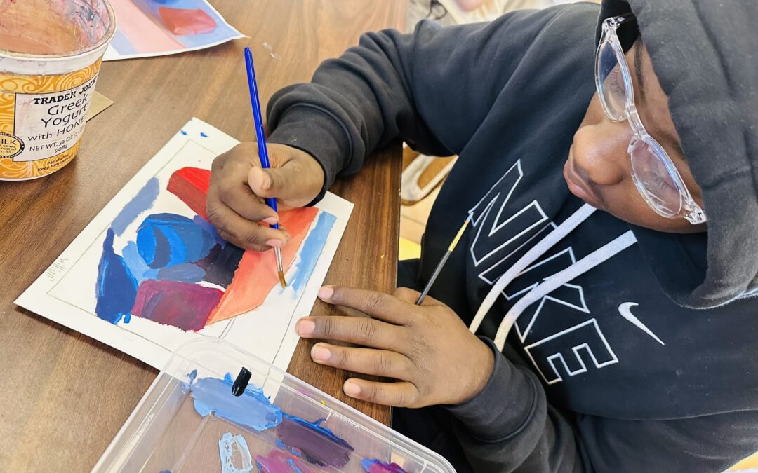 student at WAA charter arts high school painting with watercolor on a sheet of paper while seated at their classroom table